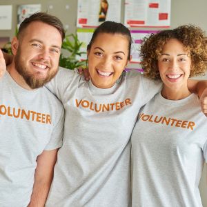 Three adult volunteers smiling with arms around each other