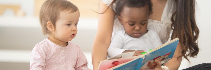 two babies sitting with adult reading a book
