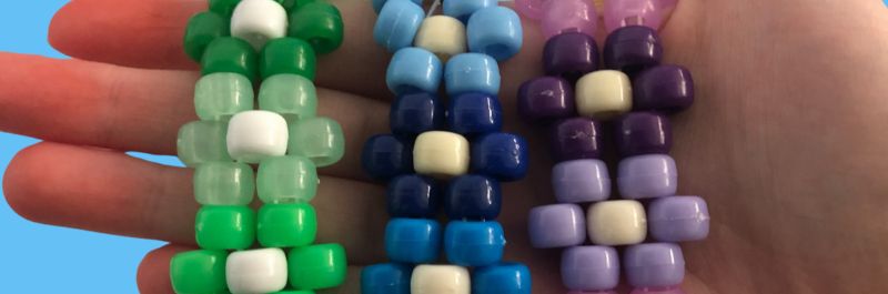 Three clower cuff bead bracelets. Green, blue and purple laid out on a person's hand. 