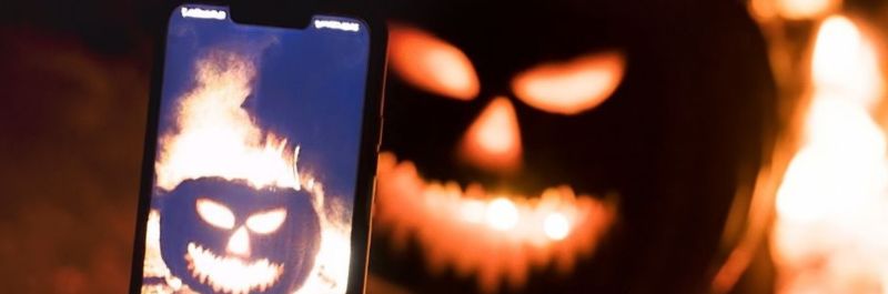 Jack-o-lantern sitting in front of a fire at night. A cell phone taking a picture of jack-o-lantern