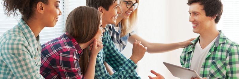 Group of young adults in casual plaid shirts, talking and smiling at each other indoors.