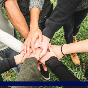 A group of hands joined together in a circle over grass, symbolizing unity.