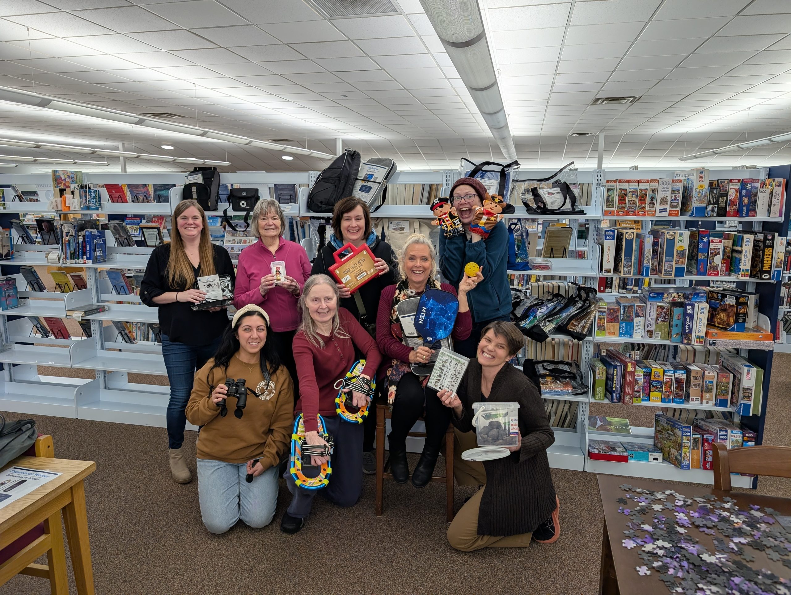 Friends of the Prescott Public Library in front of library shelves and holding various library of things items