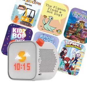 Grey cube-shaped Yoto Player with digital display surrounded by colorful themed Yoto cards for children.
